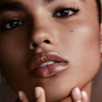 Close-up of a model's face showcasing a glossy, nude-pink lip color with a high-shine finish.