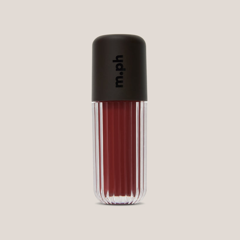 A single lip gloss bottle from the brand m.ph, featuring a ribbed clear glass body showing a deep berry red gloss and a matte black cap with the brand name printed vertically in black.