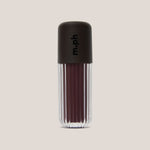 A single lip gloss bottle from the brand m.ph, featuring a dark brown ribbed cap with the brand name printed vertically, and a clear ribbed lower section showing a deep berry-brown gloss inside, set against a solid light beige background.