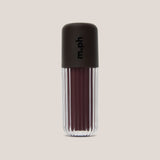 A single lip gloss bottle from the brand m.ph, featuring a dark brown ribbed cap with the brand name printed vertically, and a clear ribbed lower section showing a deep berry-brown gloss inside, set against a solid light beige background.