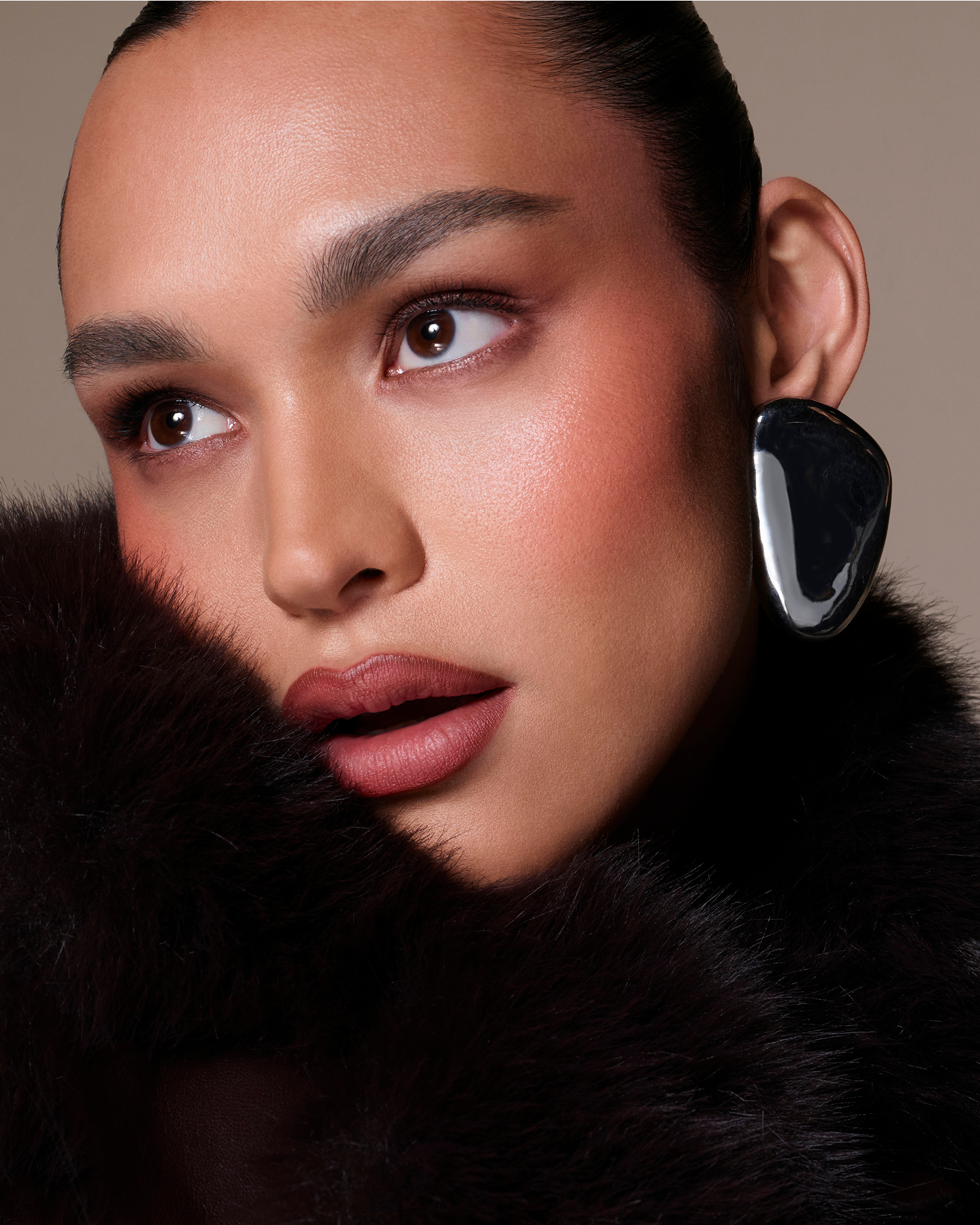 Close-up of a woman wearing a large black and silver earring with a neutral background