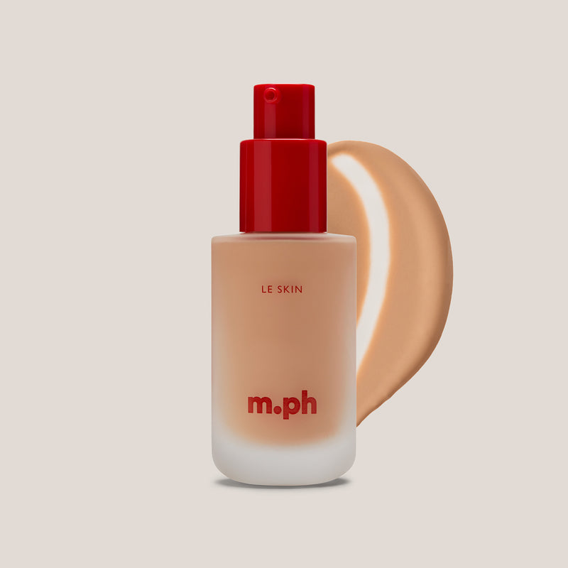 M.PH Le Skin neutral beige full coverage foundation in shade 150 with a luminous texture swatch behind the frosted glass bottle.