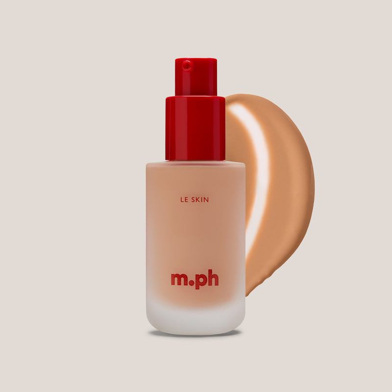 M.PH Le Skin warm beige foundation bottle in shade 160 with a smooth texture swatch behind the frosted glass packaging.