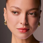 Close-up of a woman's face wearing gold hoop earrings with a neutral background