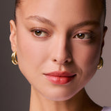 Close-up of a woman's face wearing gold hoop earrings with a neutral background