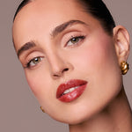 Close-up of a woman's face with red lipstick and gold earrings on a beige background