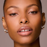 Close-up of a woman's face wearing gold hoop earrings against a neutral background