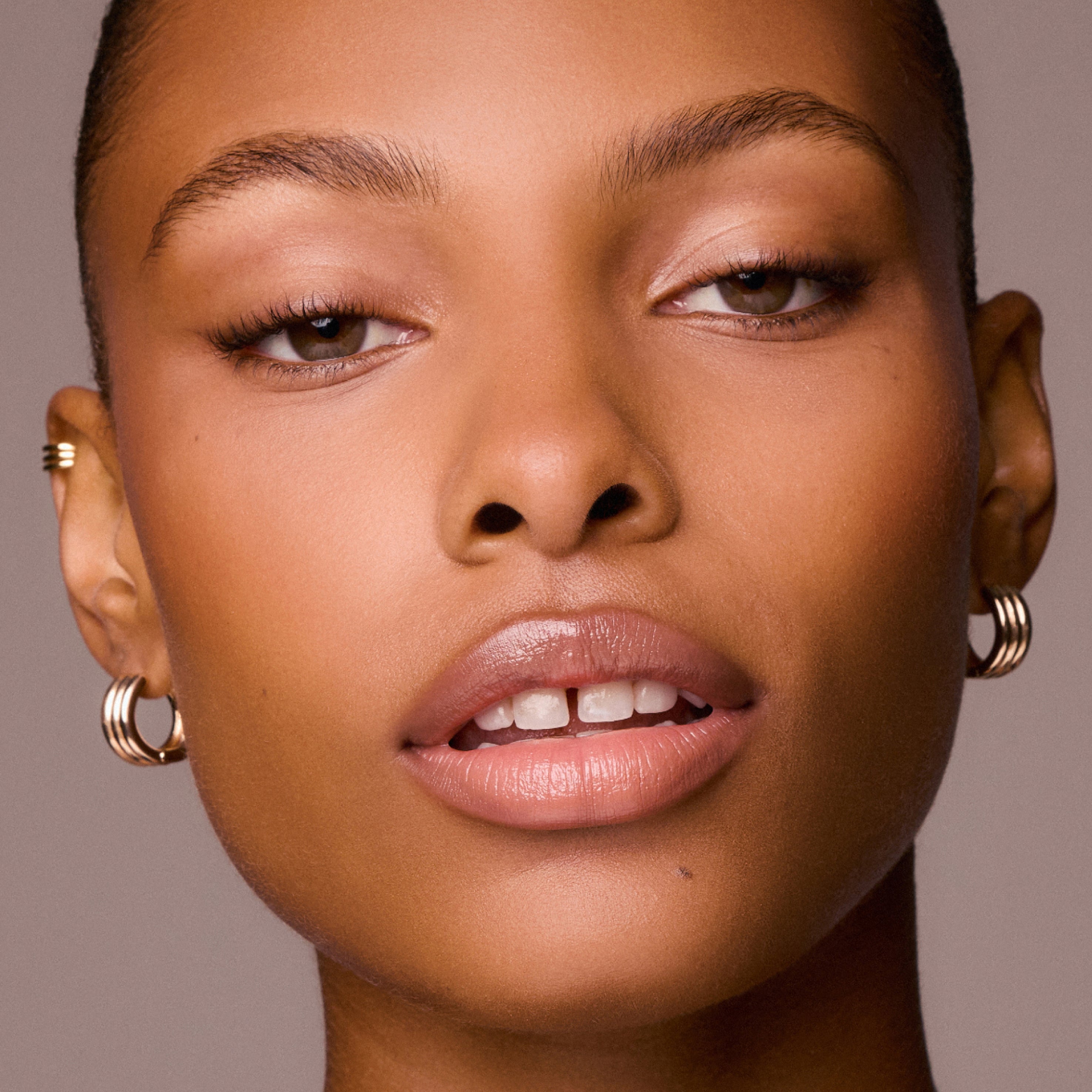 Close-up of a woman's face wearing gold hoop earrings against a neutral background