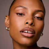 Close-up of a woman's face with gold hoop earrings against a neutral background