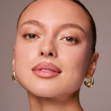 Close-up of a woman's face with gold hoop earrings on a neutral background