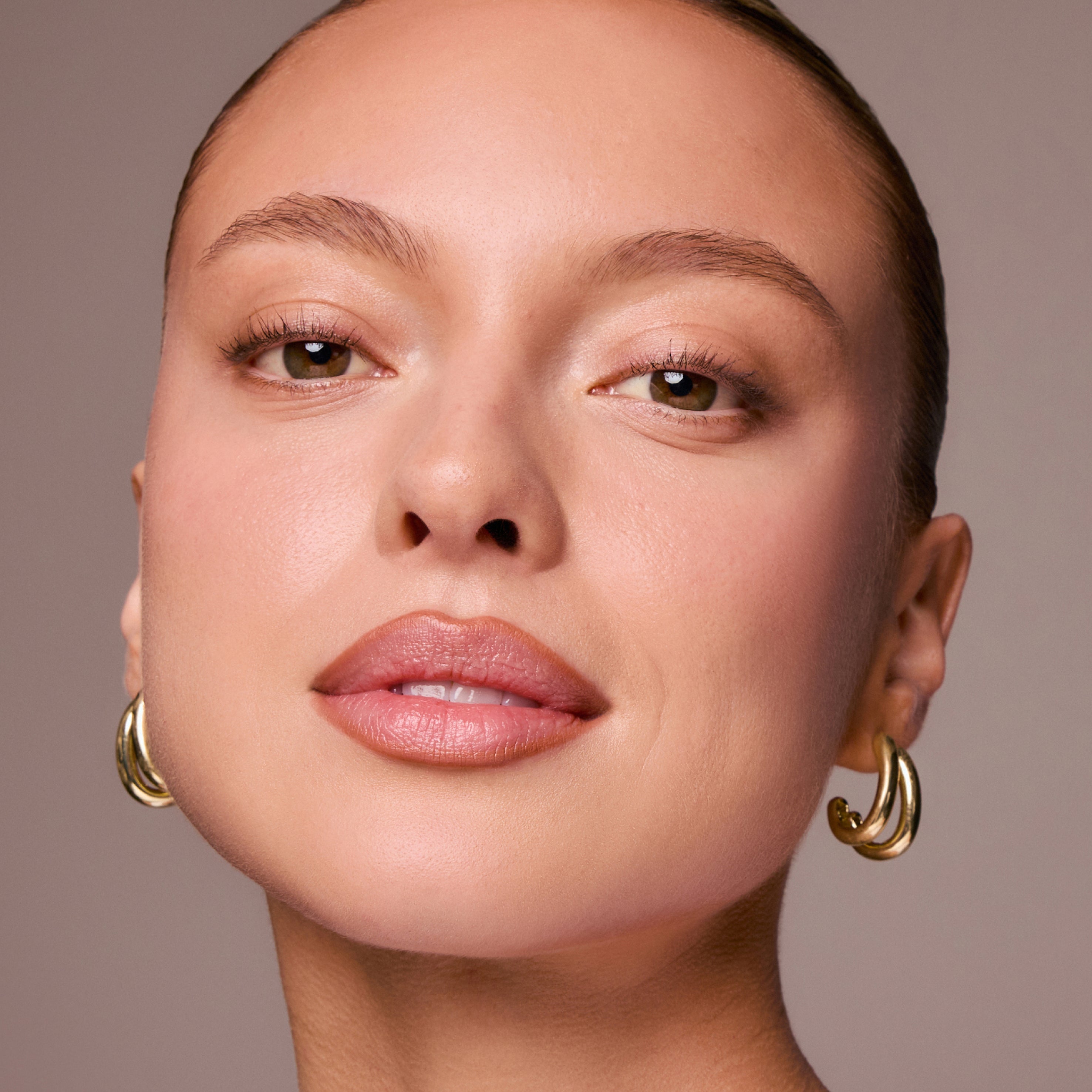 Close-up of a woman's face with gold hoop earrings on a neutral background