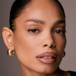 Close-up of a woman's face with gold earrings against a neutral background