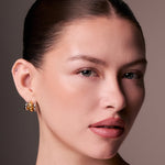 Close-up of a woman wearing gold earrings against a neutral background
