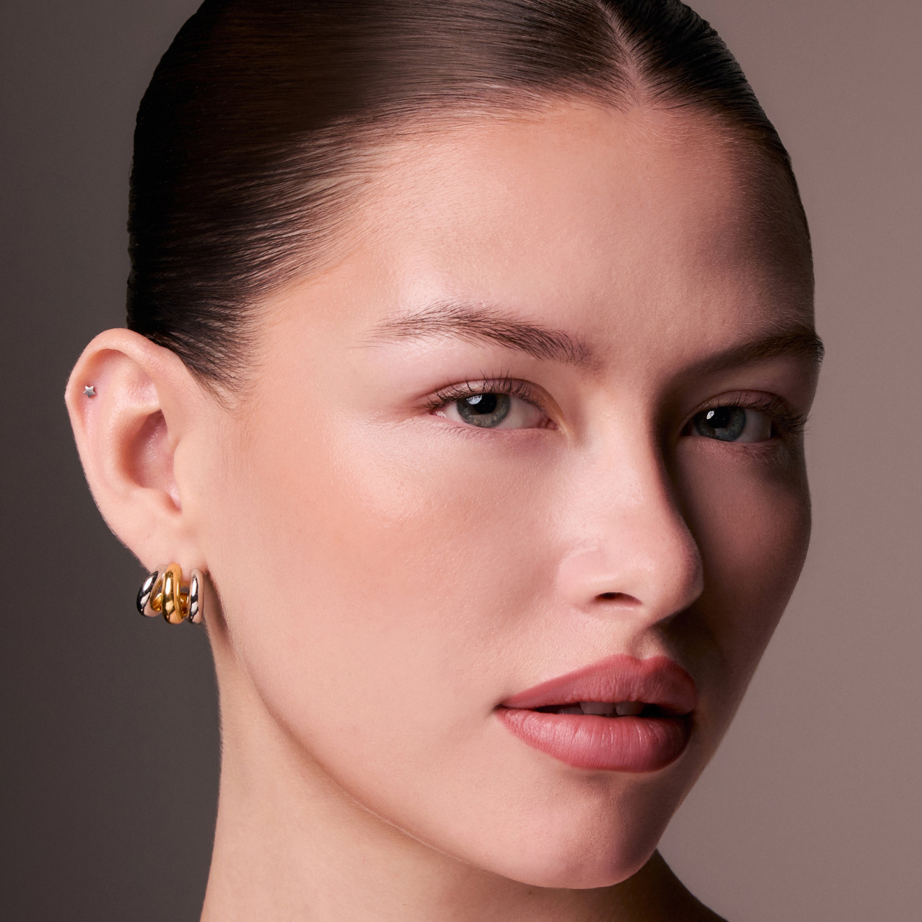 Close-up of a woman wearing gold earrings against a neutral background