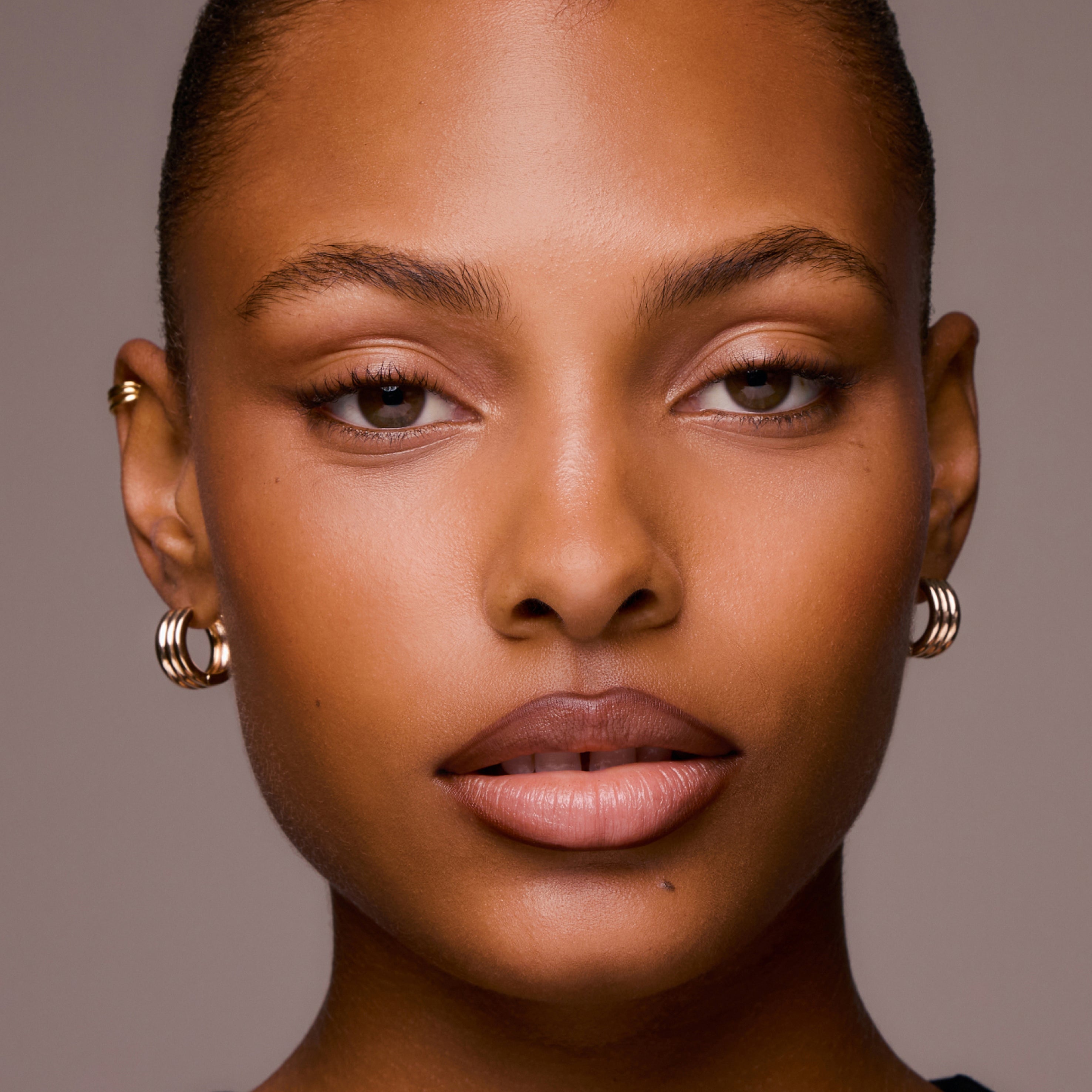 Close-up of a woman's face with gold hoop earrings against a neutral background