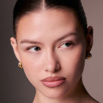 Close-up of a woman's face with gold earrings against a neutral background