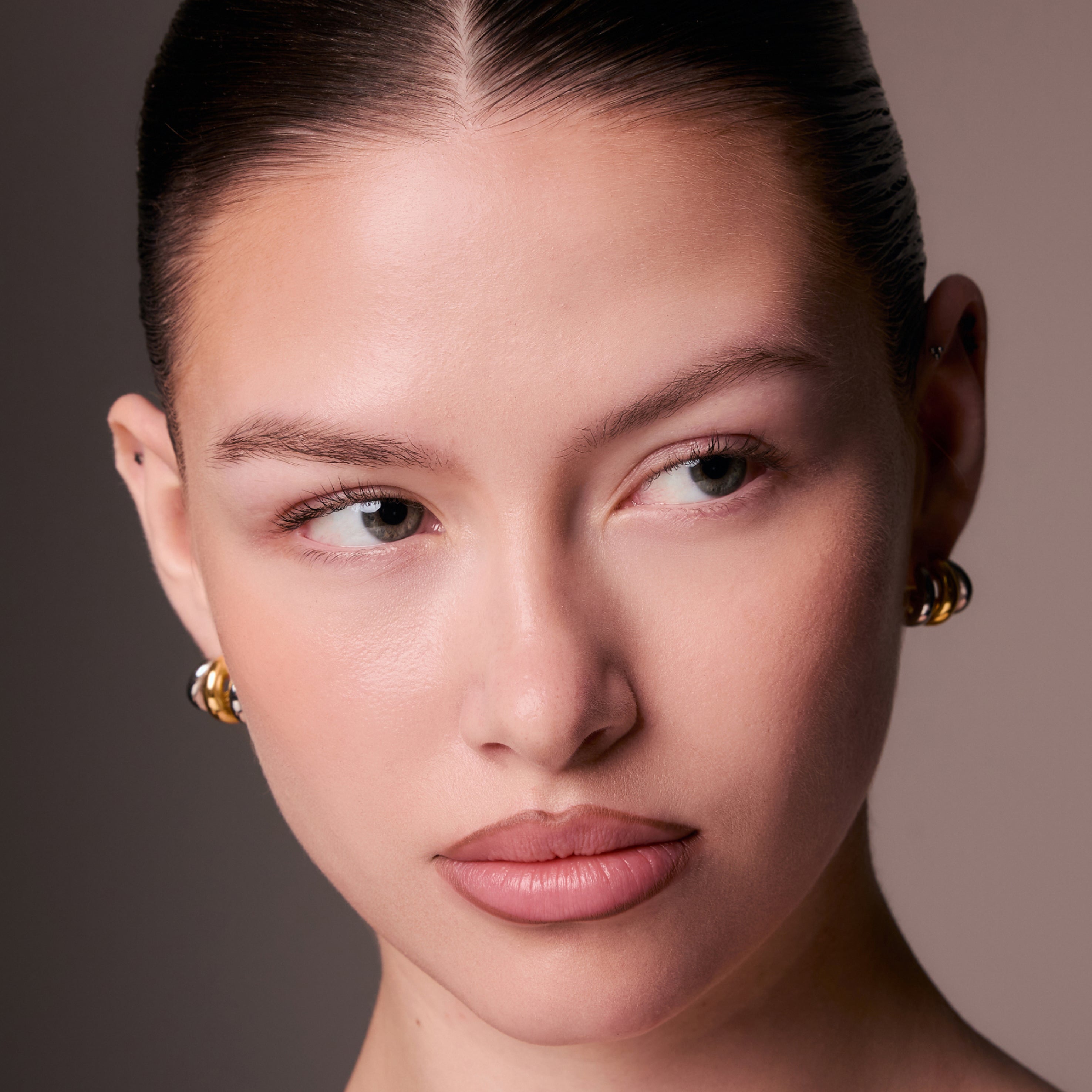 Close-up of a woman's face with gold earrings against a neutral background