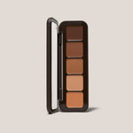 Open Underpainting face palette in tan with five cream contour and highlight shades beside mirror.